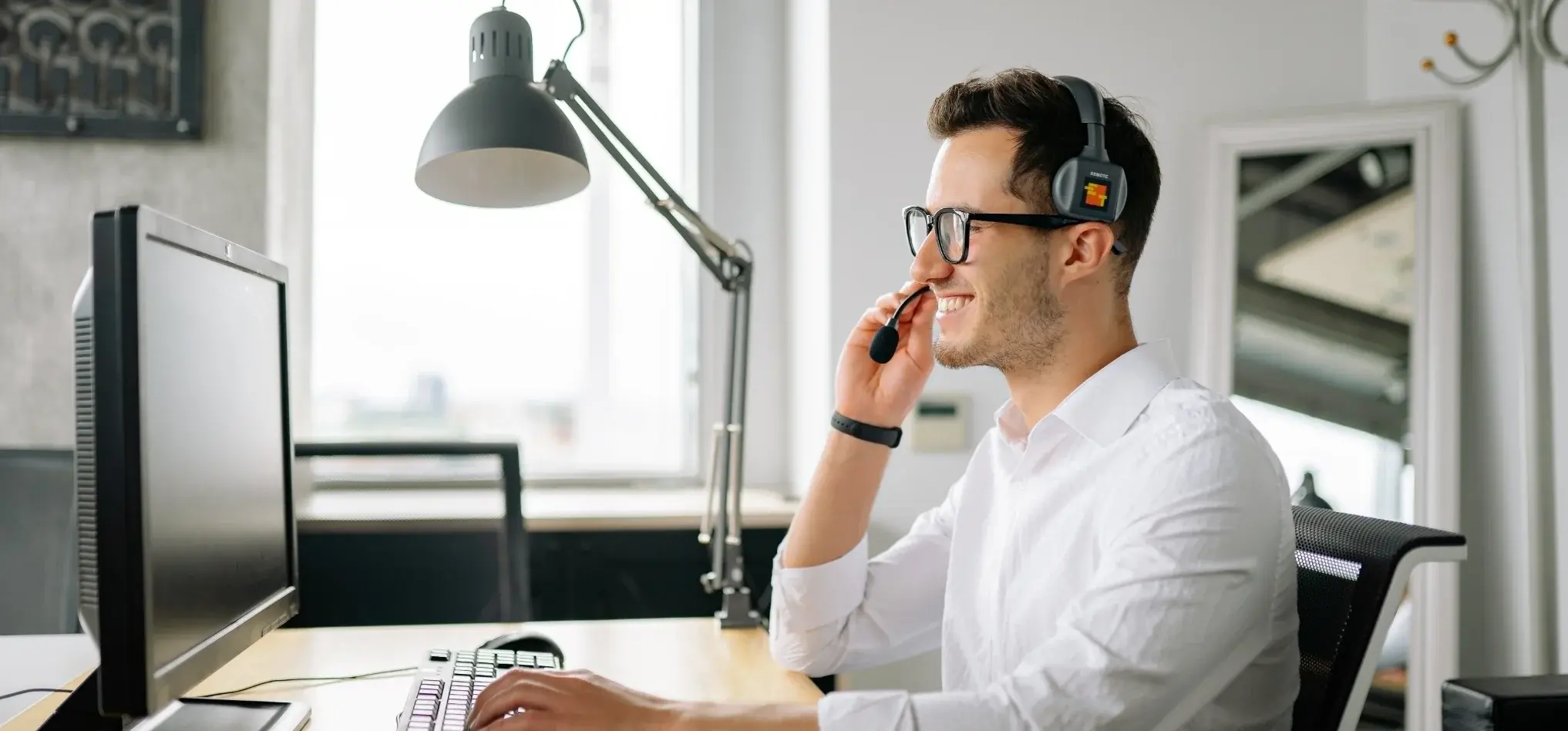 Asesor de servicio al cliente con auriculares trabajando en computadora de escritorio en oficina.